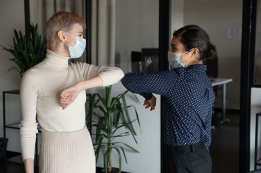 Two Women Bumping Elbows While Wearing Medical Masks